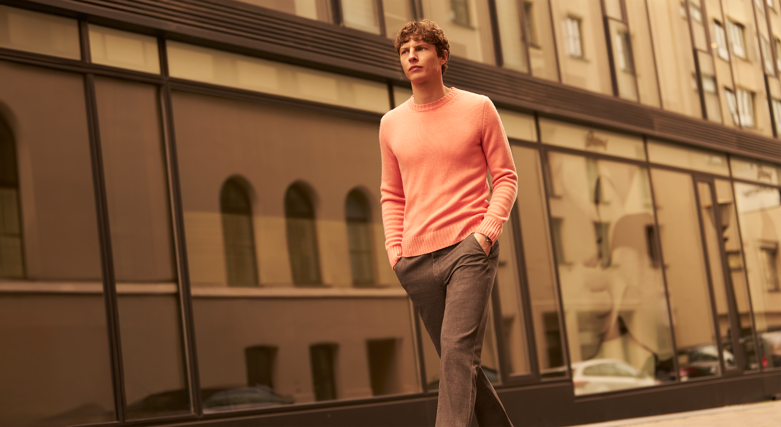 Man in a pink sweater standing in front of a reflective building facade